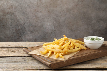 Delicious french fries with sauce on wooden table against gray background, closeup. Space for text
