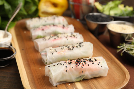 Fresh spring rolls with rice paper and sesame seeds on wooden table, closeupの写真素材