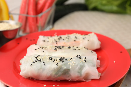 Fresh spring rolls with rice paper and sesame seeds on table, closeup