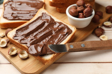 Toasts with chocolate paste, hazelnuts and knife on wooden table, closeupの写真素材