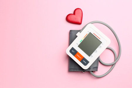 Measuring blood pressure. Sphygmomanometer and red heart figure on pink background, top view. Space...