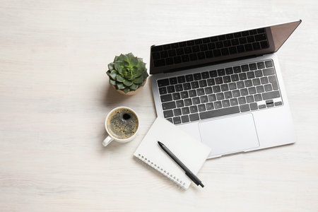 Modern laptop, notebook with pen, coffee and plant on white wooden table, flat lay