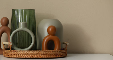 Beautiful vases and other decor on white cabinet near beige wall indoors, closeup. Space for text