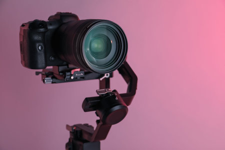 Gimbal stabilizer with camera on pink background, closeup. Space for text