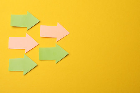 Colorful paper arrows on yellow background, flat lay. Space for text