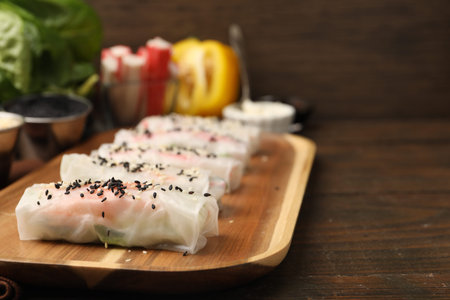 Fresh spring rolls with rice paper and sesame seeds on wooden table, closeup. Space for text