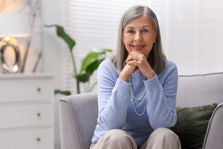 Portrait of smiling senior woman in sweater on armchair at home. Space for text