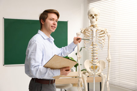 Teacher demonstrating human skeleton model in classroom. Anatomy lesson