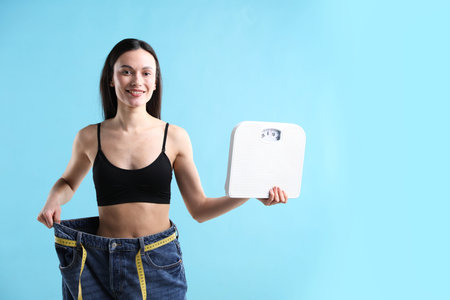 Woman with scales wearing big jeans on light blue background, space for text