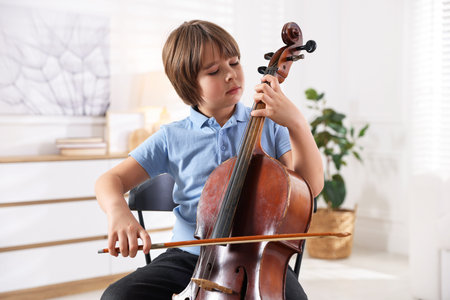 Little boy playing violoncello on chair at home