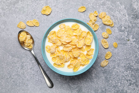 Tasty corn flakes with milk in bowl served on grey table, flat lay