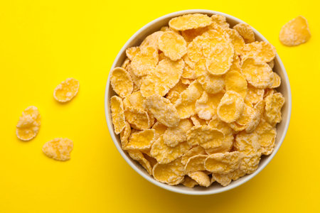 Tasty corn flakes in bowl on yellow background, top view