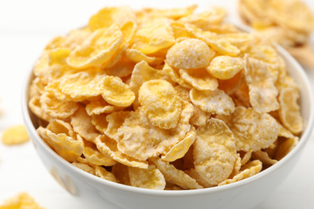 Tasty corn flakes in bowl served on white table, closeup