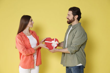 Romantic date. Man surprising his girlfriend with gift on yellow backgroundの写真素材