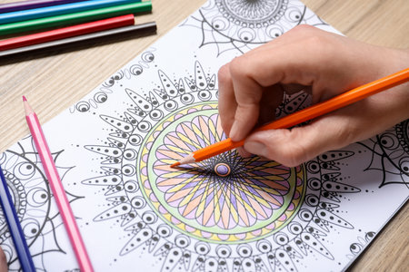 Woman coloring antistress picture with pencils at wooden table, closeupの写真素材
