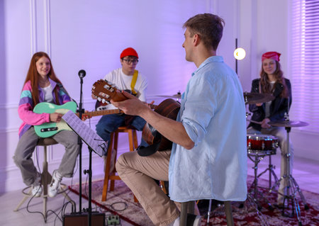 Teenage band practicing their performance with music teacher indoors