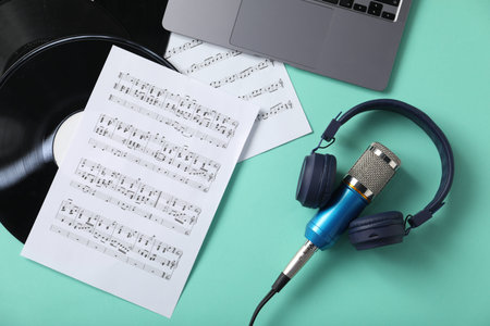 Headphones, microphone, music sheets, laptop and vinyl records on turquoise background, flat lay