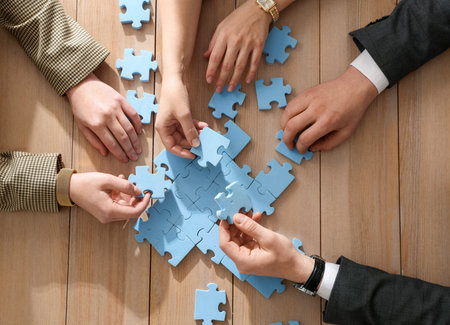 Team building. Group of businesspeople solving puzzle together at wooden table, top view