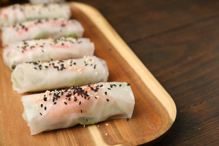 Fresh spring rolls with rice paper and sesame seeds on wooden table, closeup