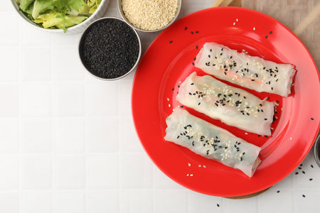 Fresh spring rolls with rice paper and sesame seeds on white tiled table, flat lay. Space for text