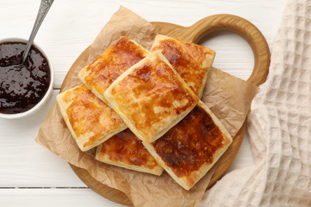 Tasty puff pastries and jam on white wooden table, flat lay