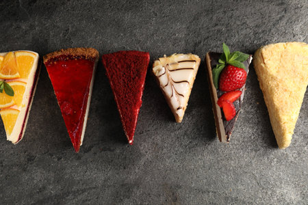 Pieces of different tasty cakes on grey table, flat lay