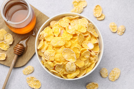 Tasty corn flakes in bowl served with honey on grey table, flat lay