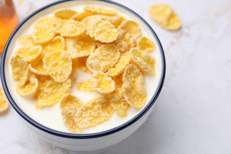 Tasty corn flakes with milk in bowl served on white marble table, closeup