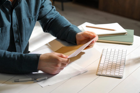 Man opening envelope with letter at white wooden table indoors, closeup