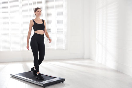 Sporty woman training on treadmill indoors, space for text