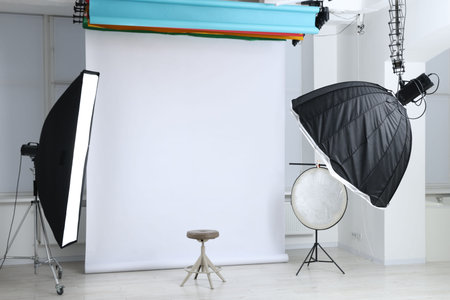 Professional lighting equipment hanging from ceiling and chair in photo studio