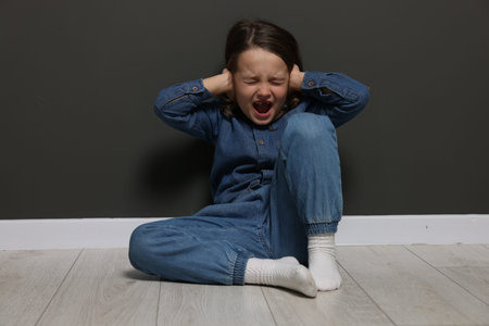 Autism. Little girl with sensory issues screaming near black wall indoors