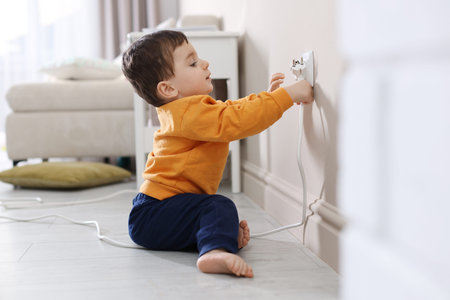 Child safety at home. Little boy taking plug out of power outlet indoors