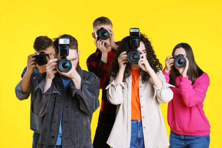 Group of photographers taking pictures with professional cameras against yellow background