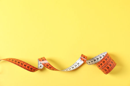 One measuring tape on yellow background, top view. Space for text