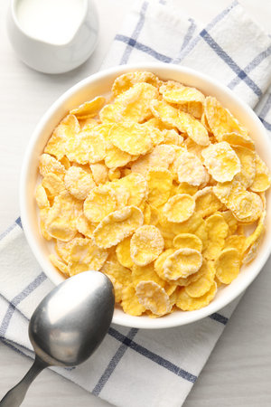 Tasty corn flakes in bowl served with milk on white wooden table, flat lay
