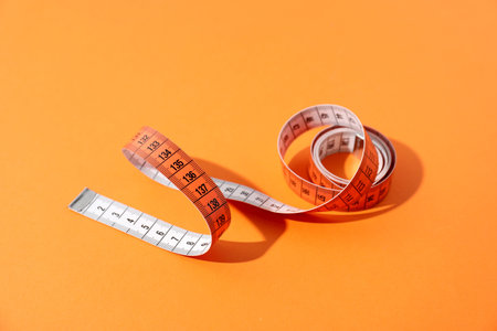 One measuring tape on orange background, closeup