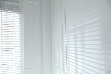 Light and shadows from window blinds falling on white wallの写真素材