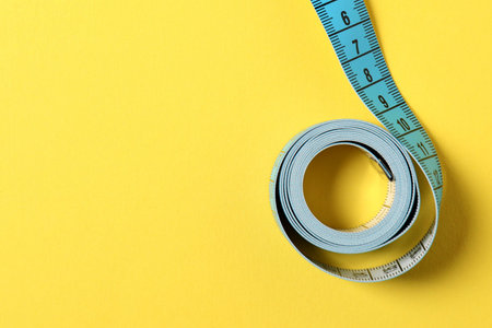 One measuring tape on yellow background, top view. Space for text