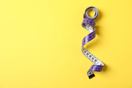 One measuring tape on yellow background, top view. Space for text