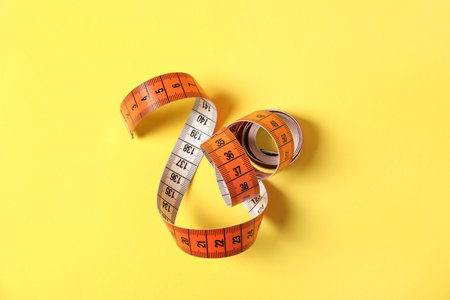 One measuring tape on yellow background, top view