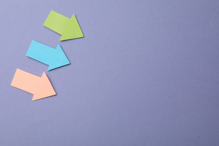Colorful paper arrows on violet background, flat lay. Space for text