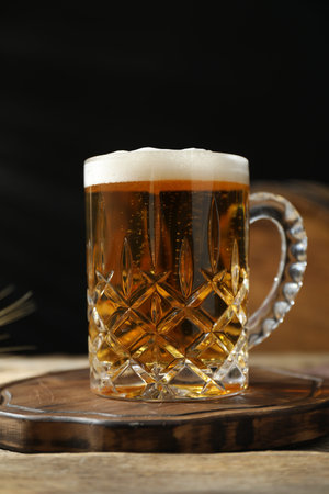 Mug with fresh beer on wooden table against dark background, closeup