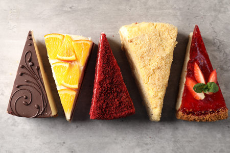 Pieces of different tasty cakes on grey table, flat lay