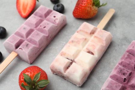 Delicious yogurt popsicles, blueberries and strawberries on grey table, closeup