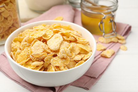 Tasty corn flakes in bowl served on white wooden table, closeup