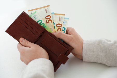 Man putting euro banknotes into wallet at white table, closeup