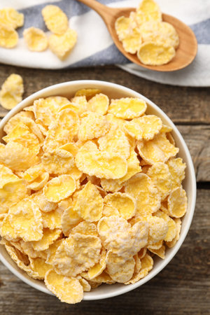Tasty corn flakes in bowl and spoon on wooden table, top view
