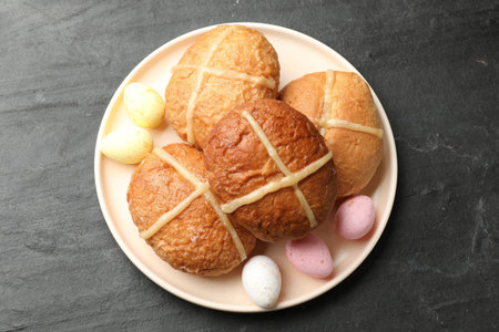 Delicious hot cross buns and colorful candies on dark textured table, top view