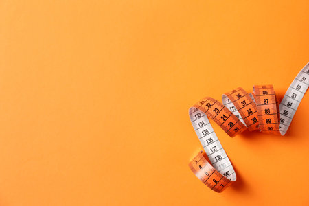 One measuring tape on orange background, top view. Space for text